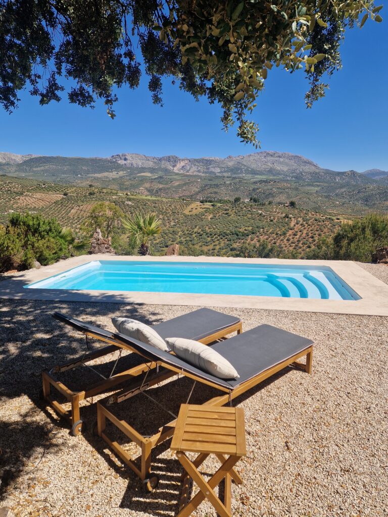 Swimming pool with sun loungers overlooking olive groves and mountains in rural Andalusia, southern Spain, symbolizing slow travel and freedom