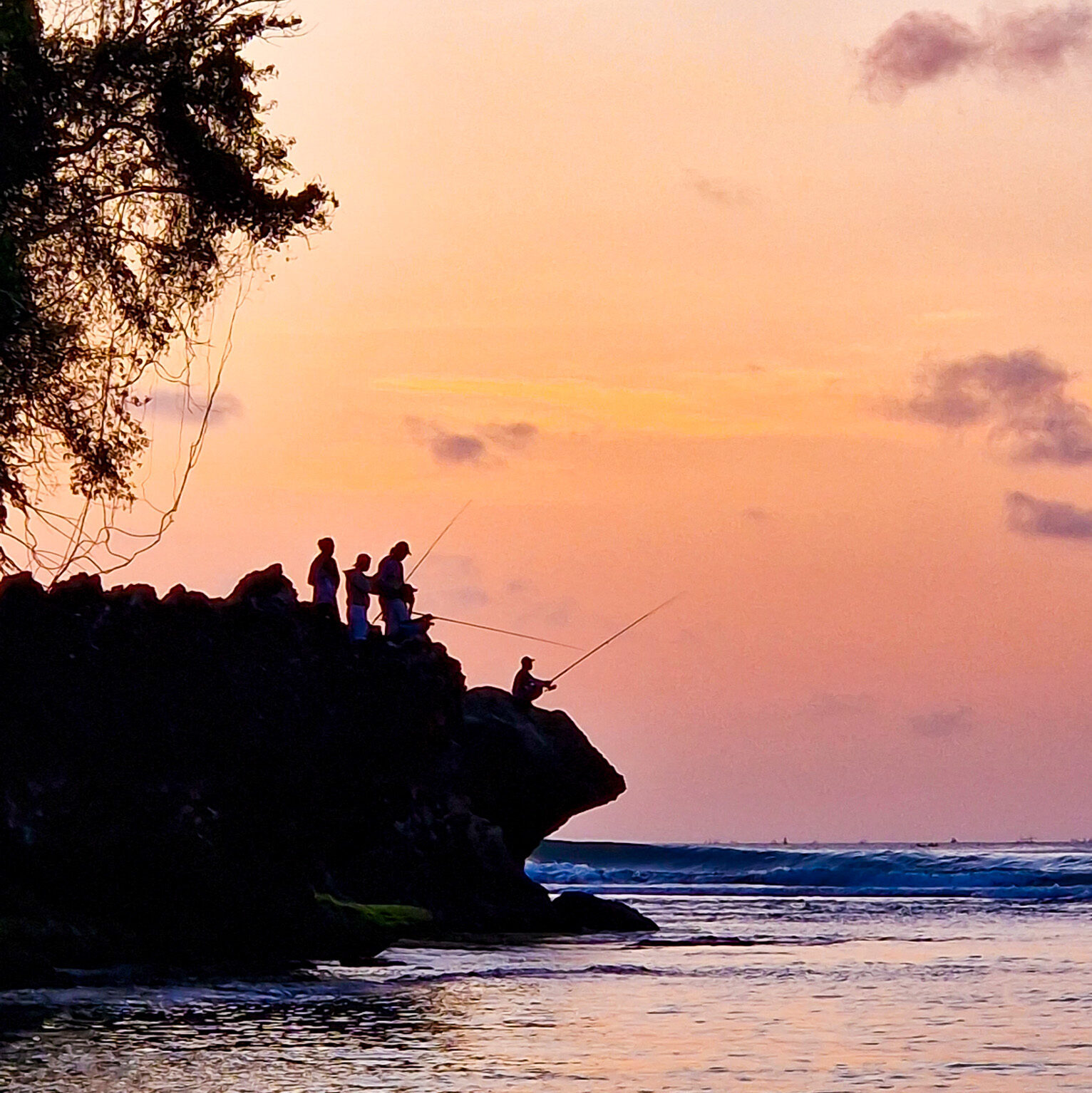 Local fishermen standing on coastal rocks at sunset during slow travel by the ocean